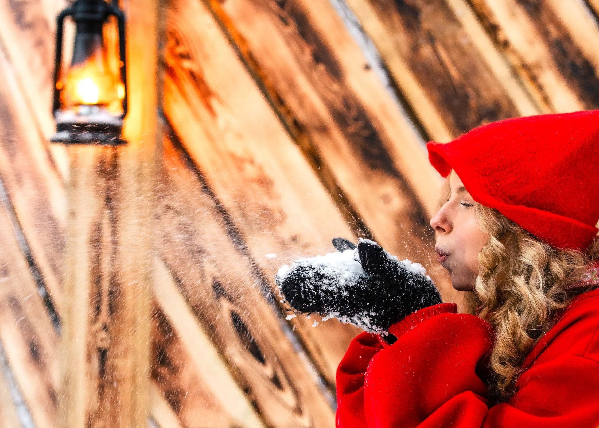 A child in a red hood blowing fresh snow from her mittens