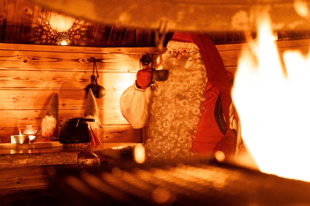 Santa Claus with a cup of coffee by the open fire