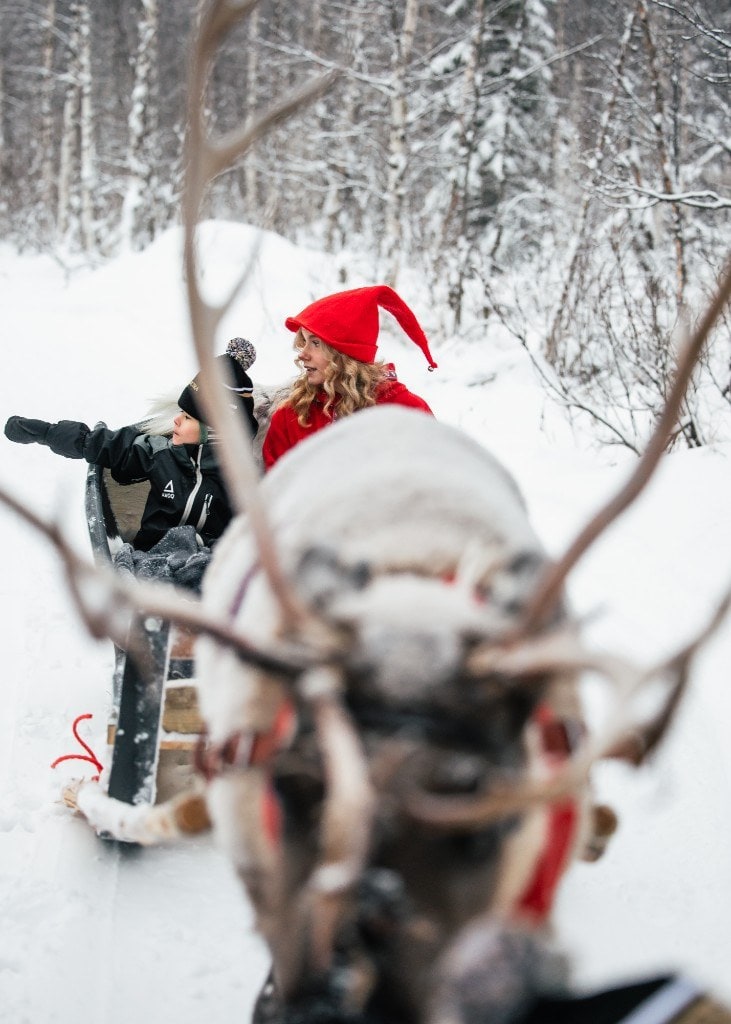 A child and an elf in a reindeer sleigh, seen past the reindeer's antlers